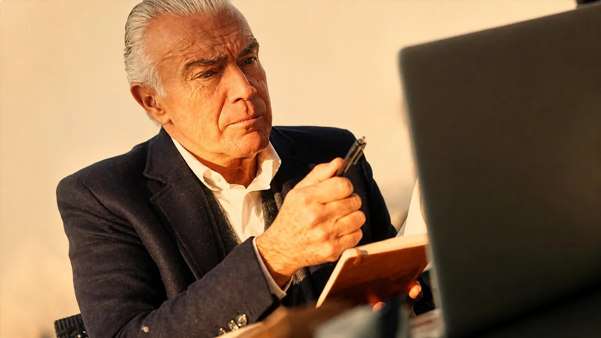 Senior investor checking smartphone by laptop